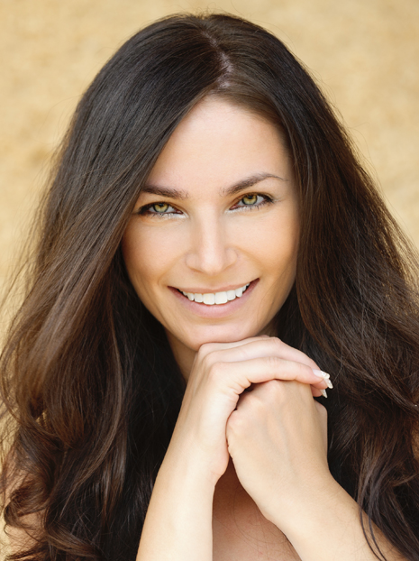 Portrait of young charming cheerful woman propping up her face against beige background.